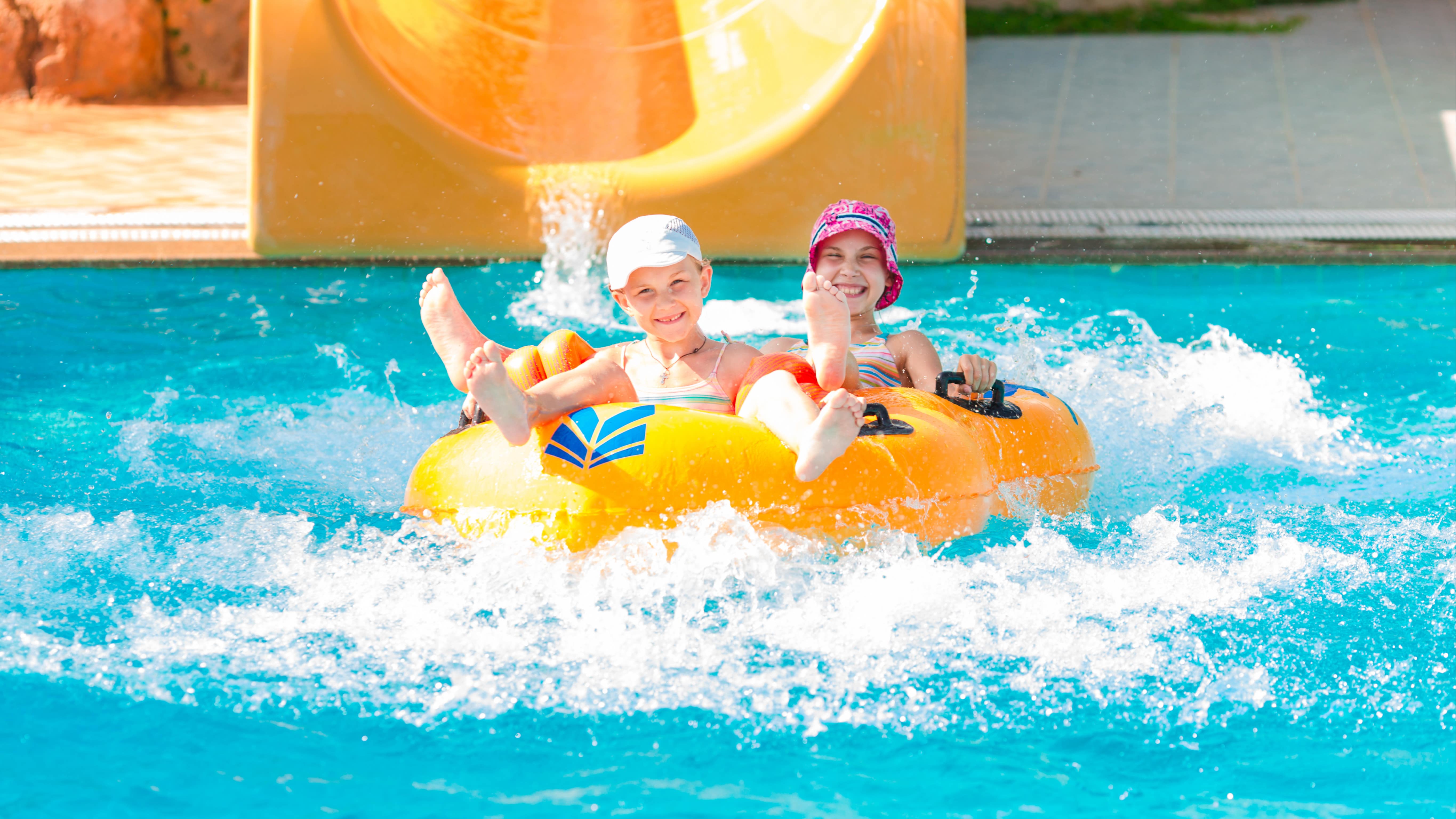Deux fillettes dans une piscine avec une grosse bouée, au bas d’un toboggan aquatique
