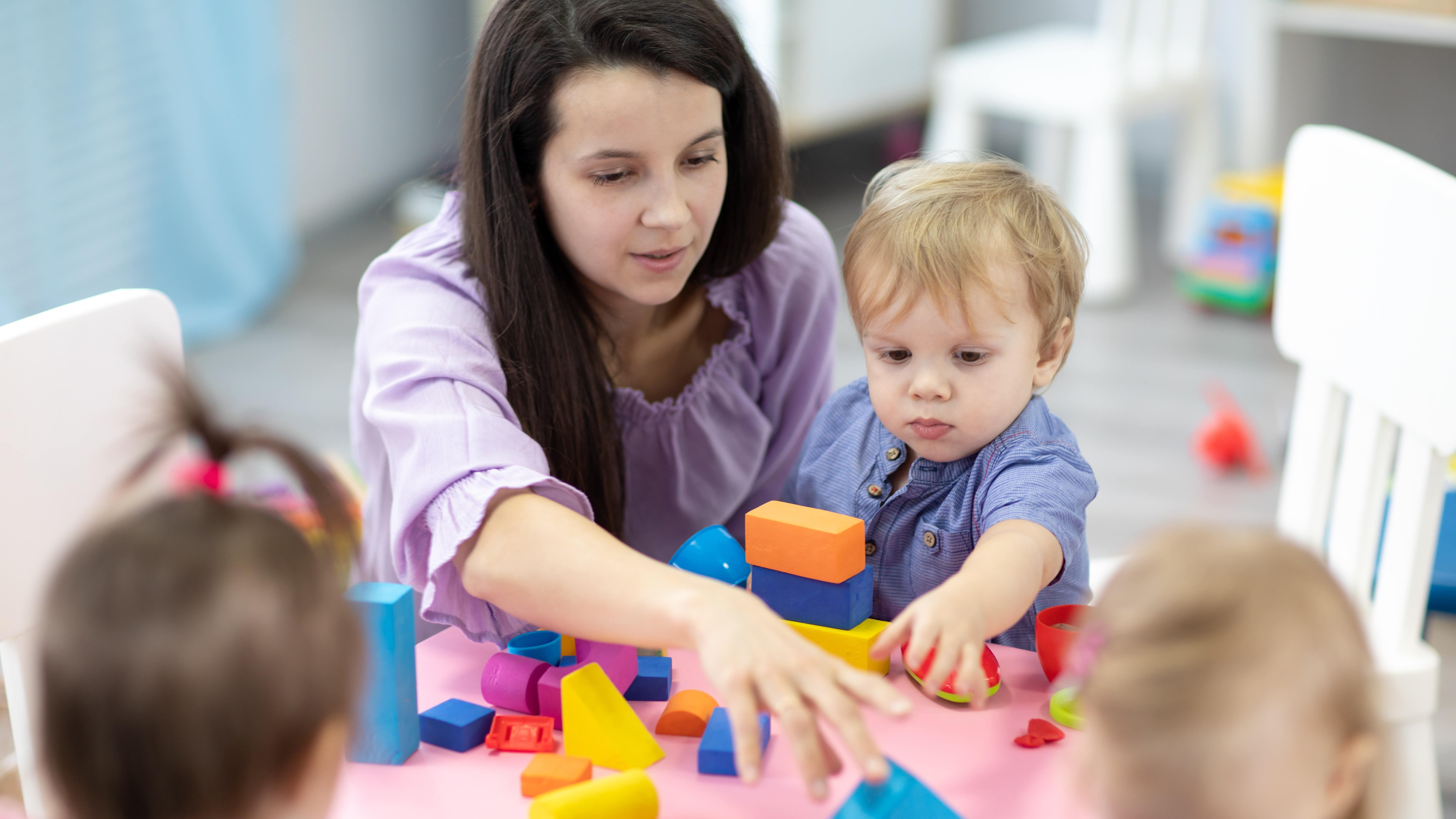 Une femme et des enfants autour d’une table où se trouve des jeux de construction