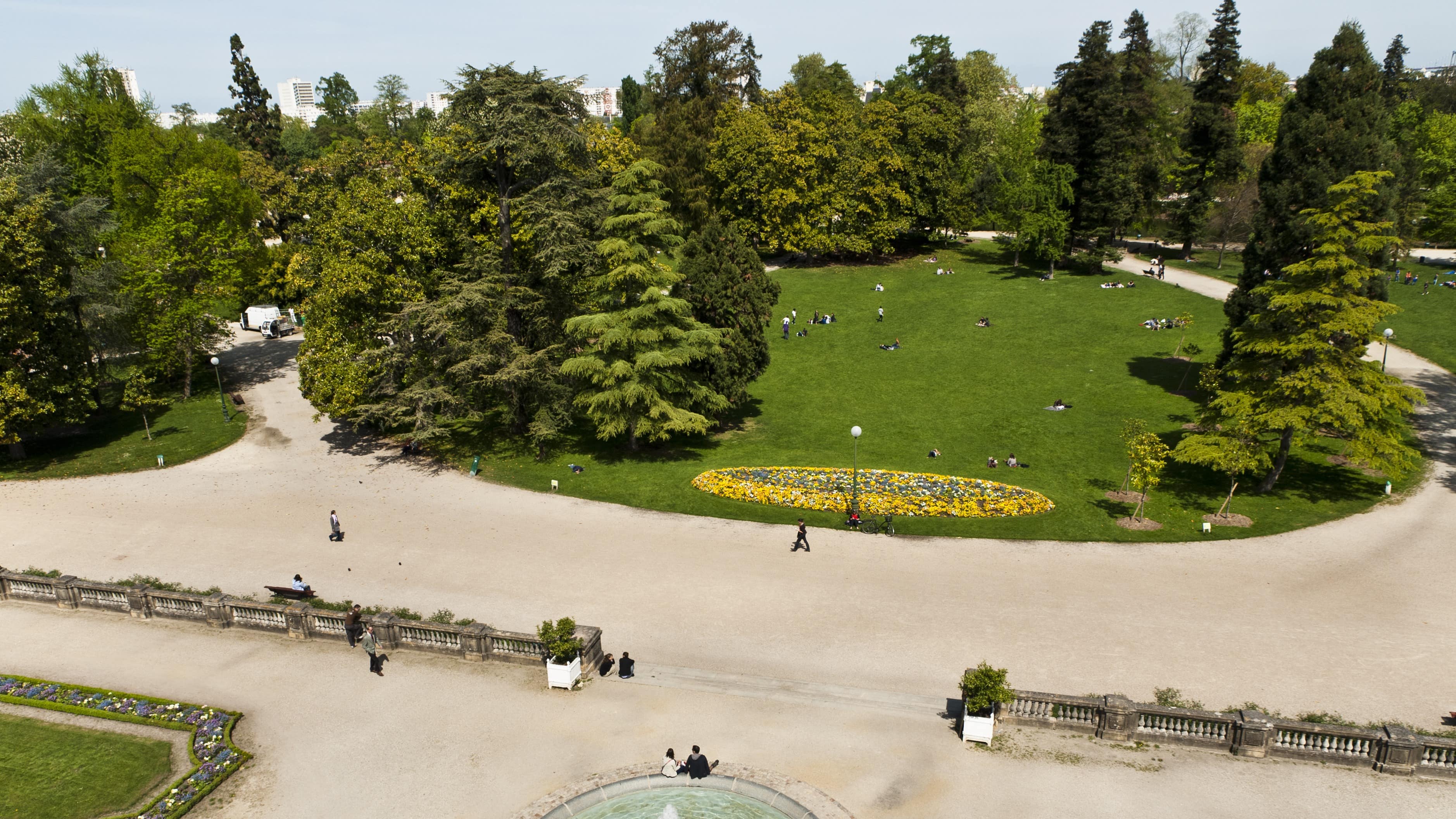 Vue aérienne du jardin public de Bordeaux : fontaine, parterres de fleurs, conifères et promeneurs installés dans l’herbe