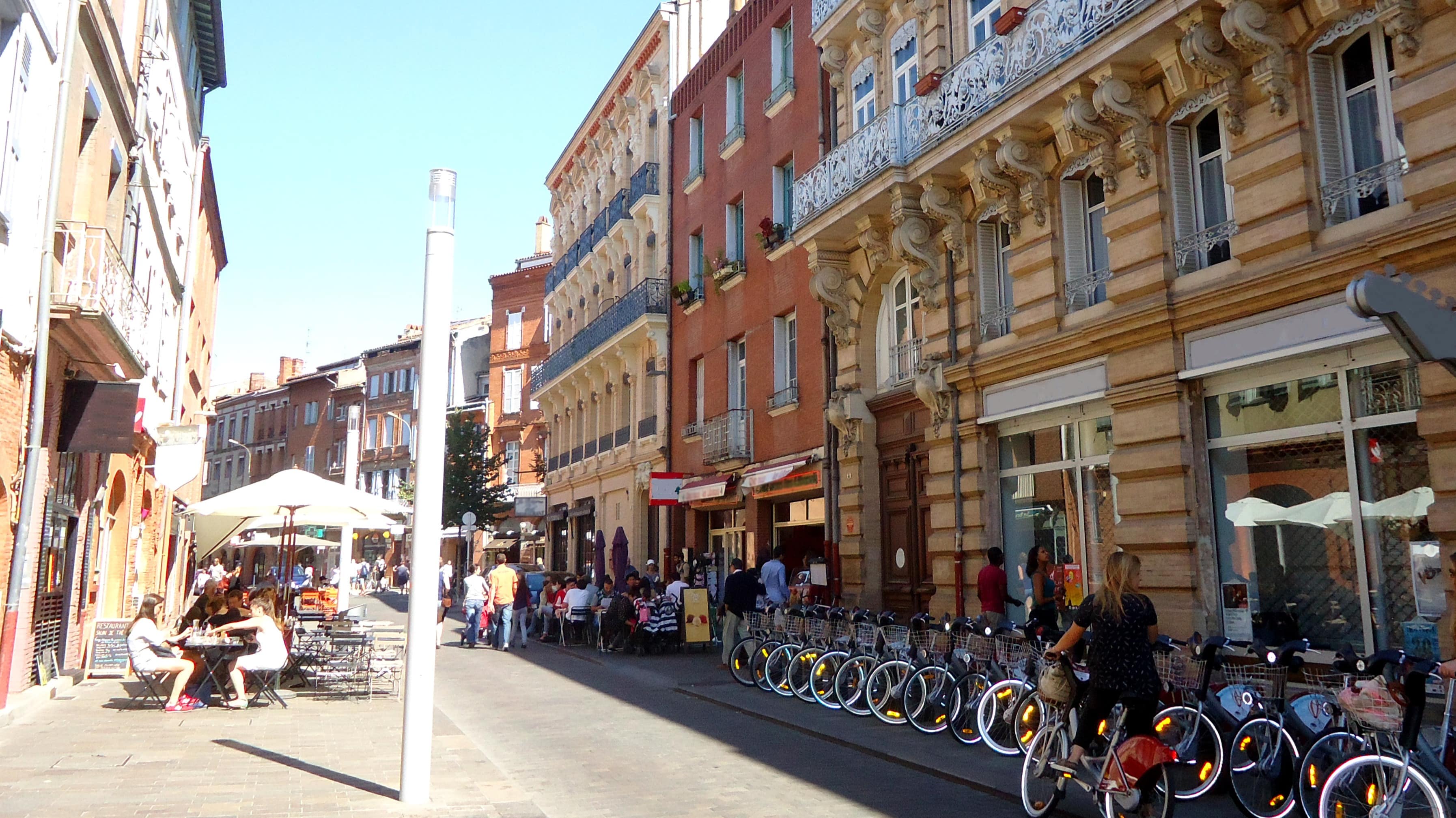 Une rue animée de Toulouse avec des vélos et des gens installés aux terrasses des cafés